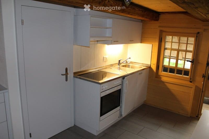 Compact kitchen with white cabinets, a built-in oven, a sink with a faucet, and a window with wooden framing.
