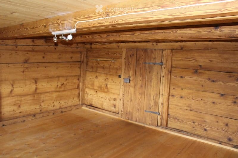 Empty wooden room with exposed wooden walls, ceiling, and floor. Features built-in wooden cabinets with metal handles and a small light fixture on the wall.