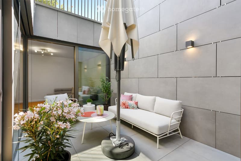Modern balcony with white sofa, small table, umbrella, and decorative plants.