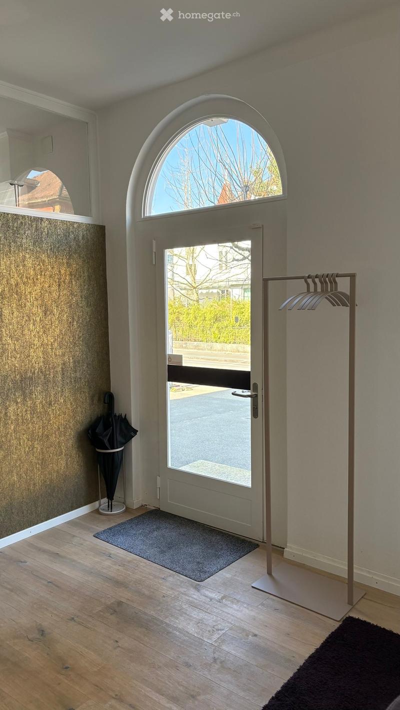 Entrance hallway with wooden flooring, a large arched window above the door, a coat rack, and an umbrella stand.