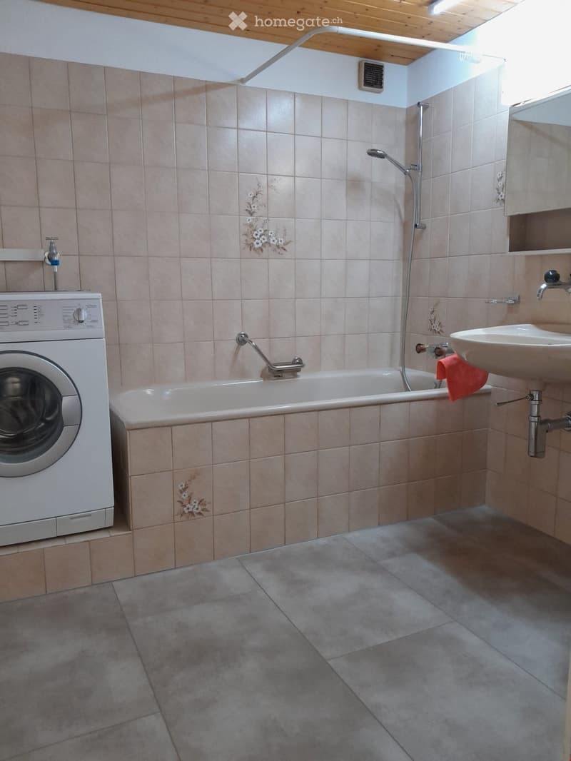 Bathroom with beige tiled walls, a bathtub, a sink, and a washing machine. Features a floral tile design and a window for natural light.