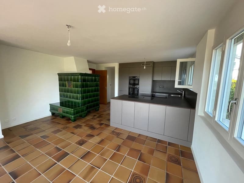 Modern kitchen with grey cabinets, black countertop, built-in oven, sink, and a green tiled stool.