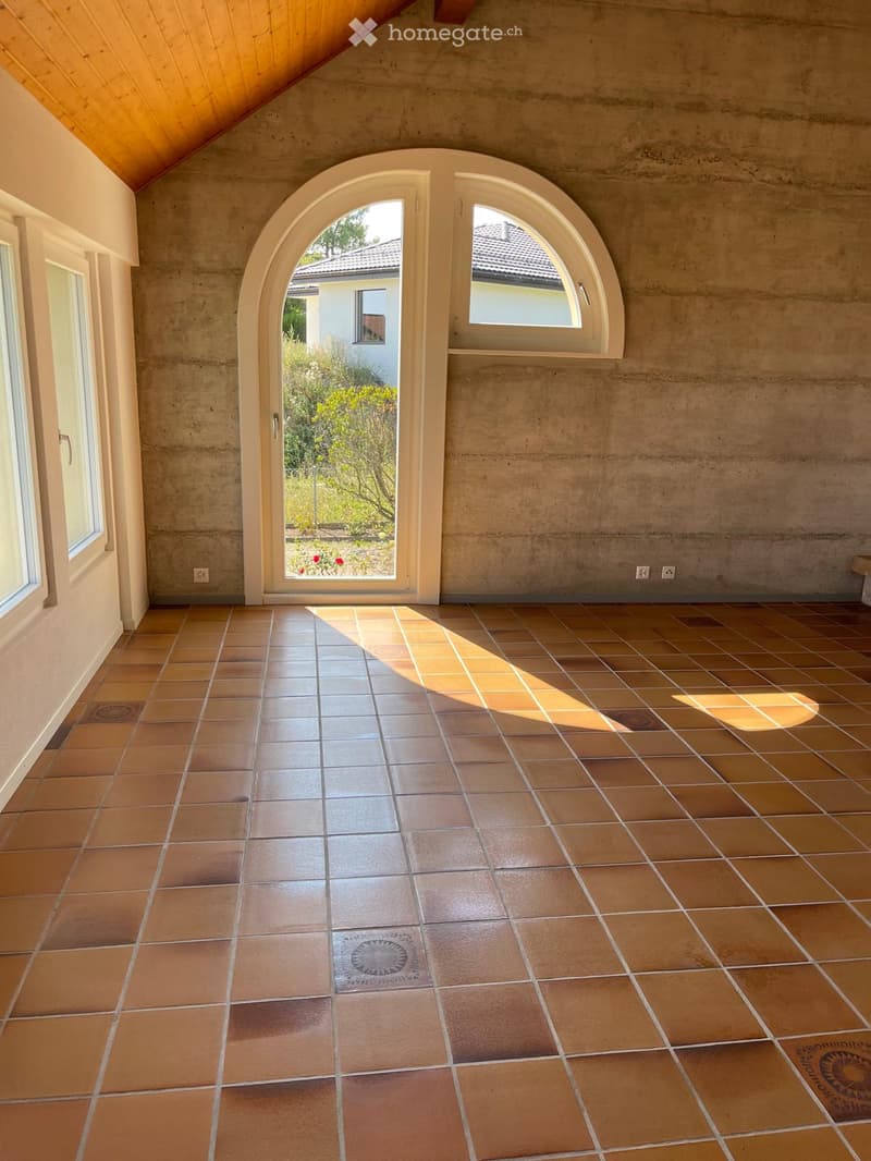 Empty room with concrete walls, tiled floor, and large arched windows allowing natural light. The space is unfurnished and features a clean, minimalist design.