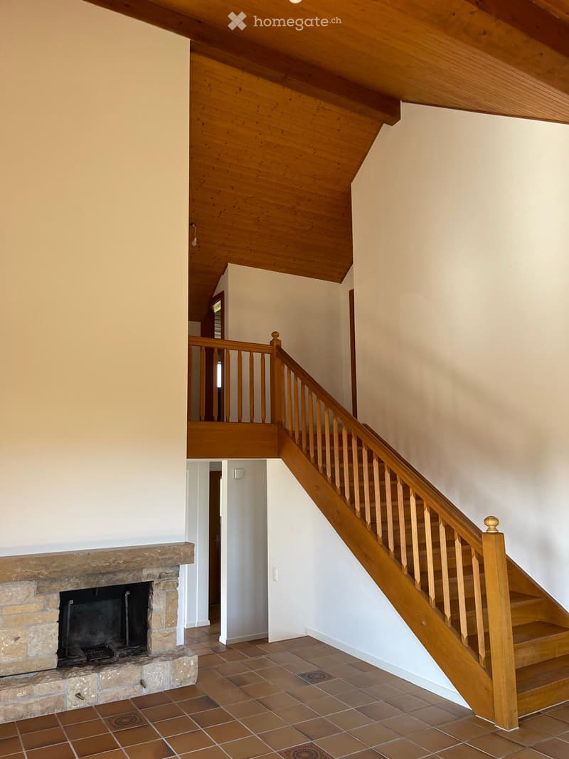 Wooden staircase with a wooden railing leads to an upper level. A stone fireplace is visible on the left side of the hallway.