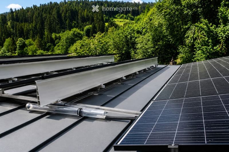 Roof with solar panels and a retractable awning system, surrounded by lush green forest and hills.