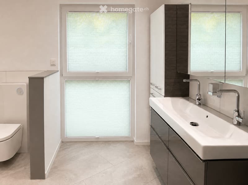 Modern bathroom with a large window, white sink with chrome faucet, toilet, and dark cabinetry.