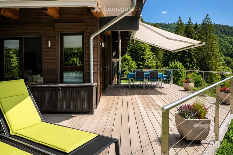 Wooden deck with lounge chairs, dining area, and potted plants, overlooking a forested landscape.