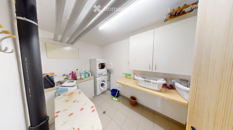 Well-lit bathroom with a washing machine and dryer, sink, mirror, cabinet, laundry baskets, ironing board, and cleaning supplies.