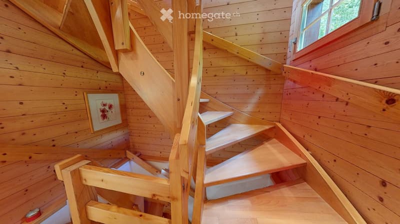 Wooden staircase with white steps and handrails, leading up to a landing with a window and a framed picture on the wall.