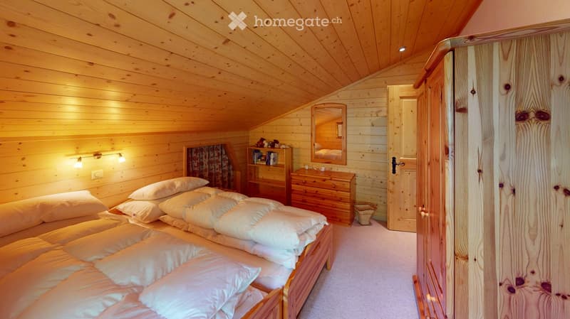 Cozy wooden bedroom with a large bed, nightstand, mirror, wardrobe, and warm lighting.