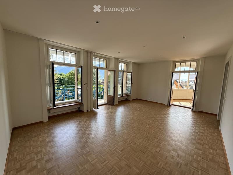 Empty room with wooden herringbone flooring, large windows, and open doors leading to balconies.
