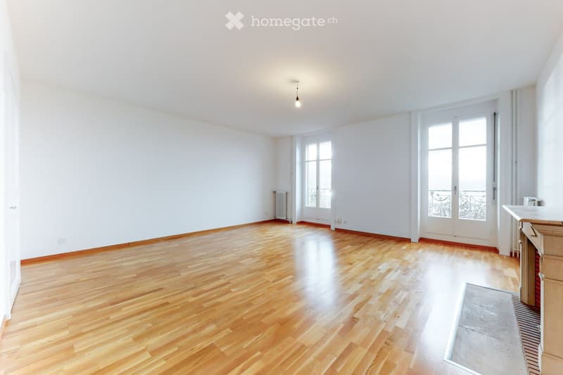 Empty room with wooden flooring, white walls, large windows, and a radiator. No furniture or equipment present.