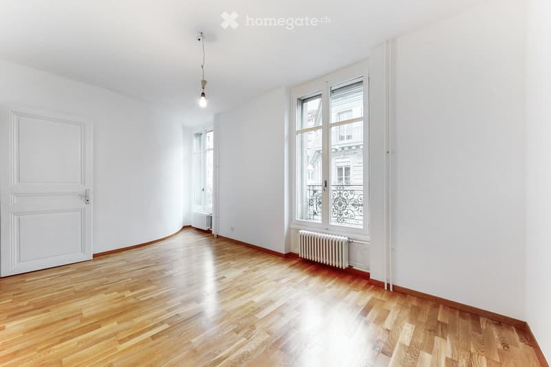 Empty room with wooden flooring, white walls, large windows, and radiators. No furniture or equipment present.