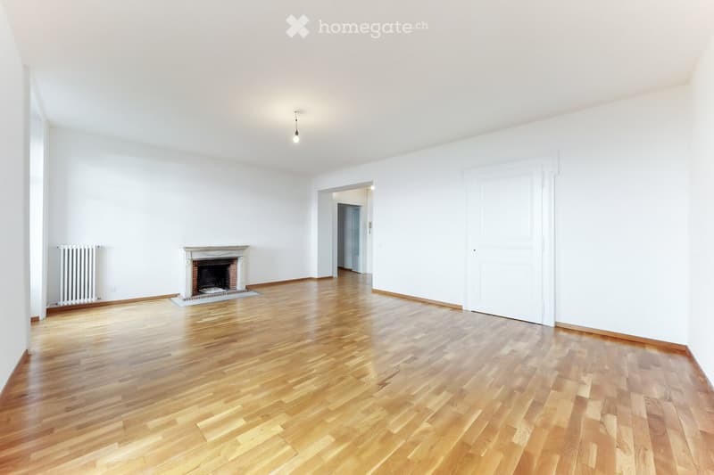 Empty room with wooden flooring, white walls, and a fireplace.