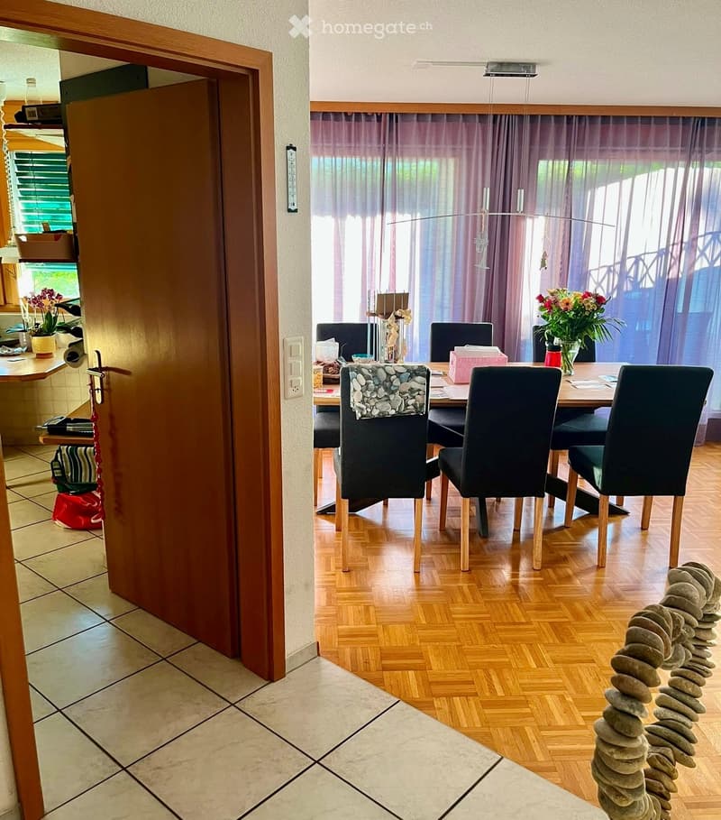 Dining area with wooden floor, dining table, chairs, flower vase, and a decorative stone sculpture on the floor.