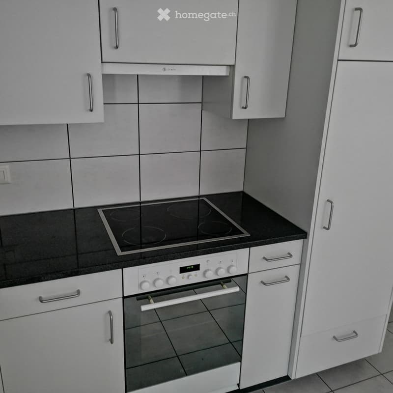 Modern kitchen with white cabinets, black countertop, induction cooktop, and built-in oven.