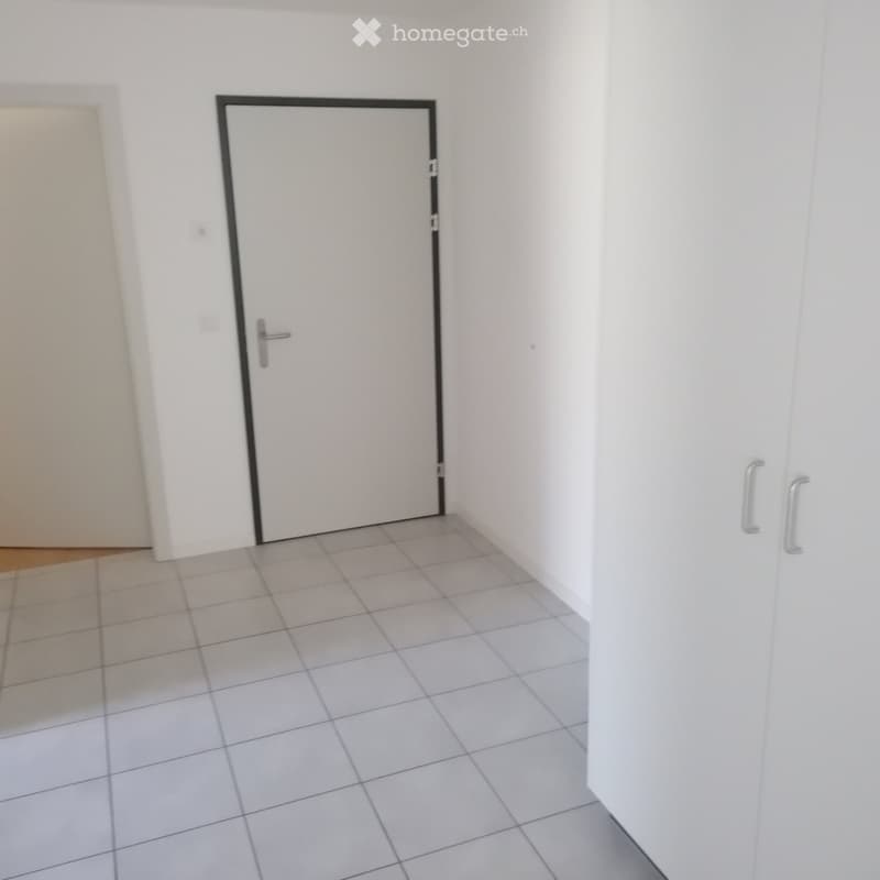 Empty hallway with white tiled floor and white walls, featuring a closed white door with a silver handle.