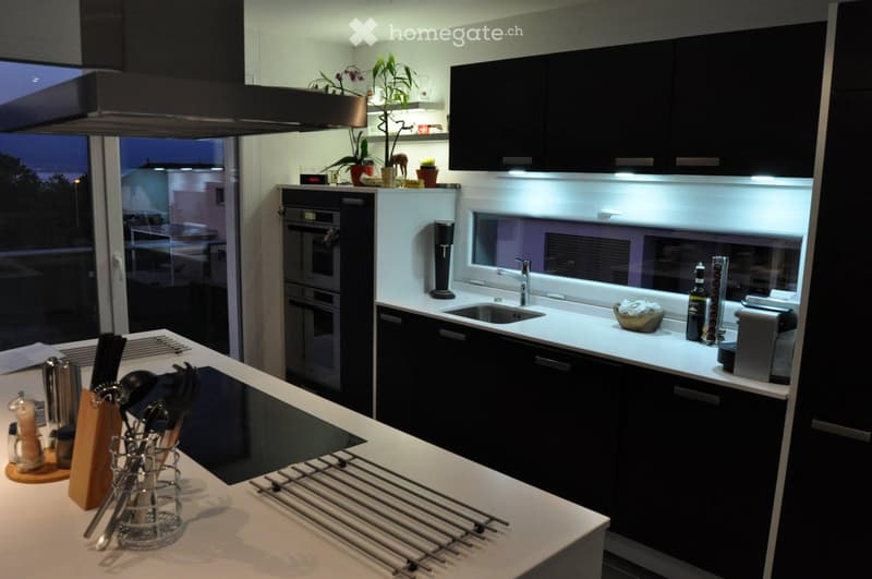 modern kitchen with black cabinets, white countertops, induction cooktop, oven, sink, faucet, plants, and a window with a view