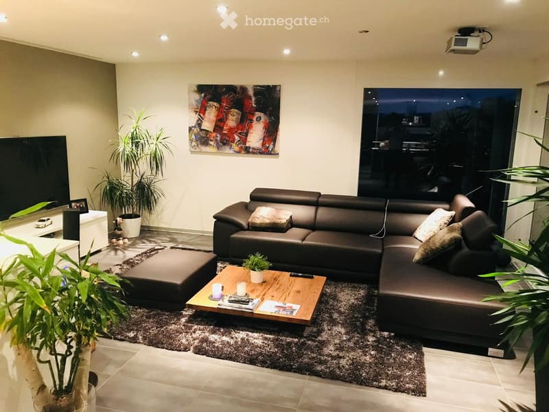 Living room with a black leather sofa, a wooden coffee table, a flat screen TV, a carpet, and potted plants