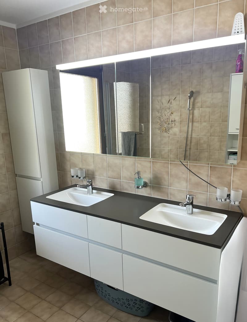 Modern bathroom with double sink vanity, white cabinets, black countertop, and large mirror with built-in lighting.