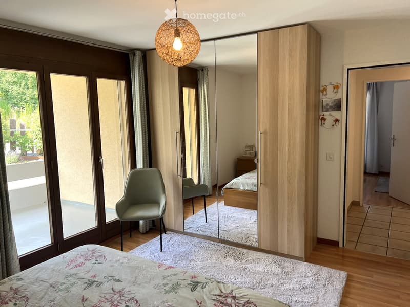 Modern bedroom with wooden flooring, large mirror wardrobe, a green armchair, and a bed with floral bedding.