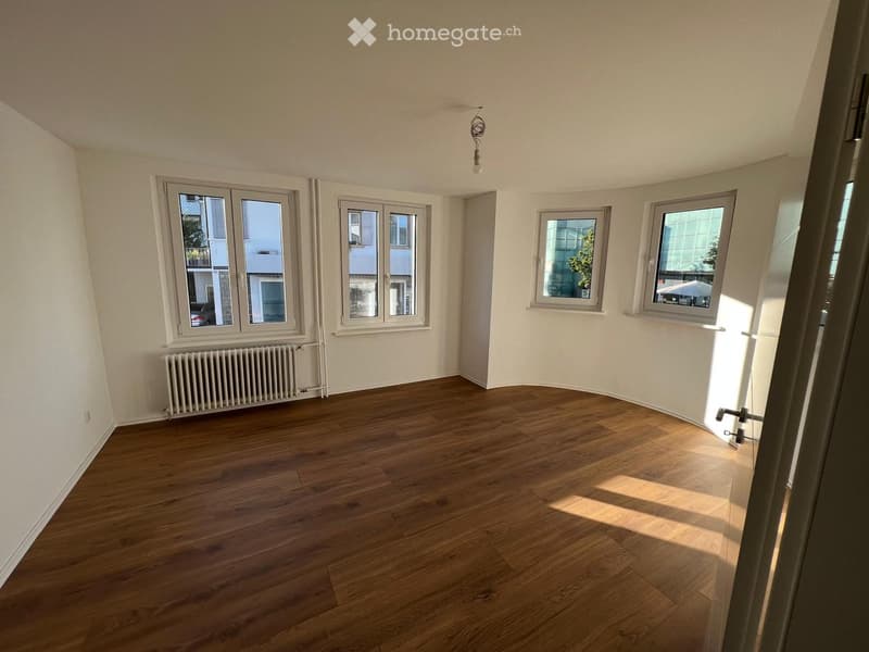 Empty room with wooden flooring, white walls, multiple windows, radiator, and visible light fixture on the ceiling.
