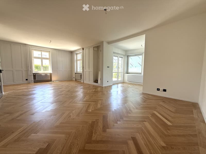 Empty room with wooden parquet flooring, white walls, large windows, and radiators. No furniture or equipment present.