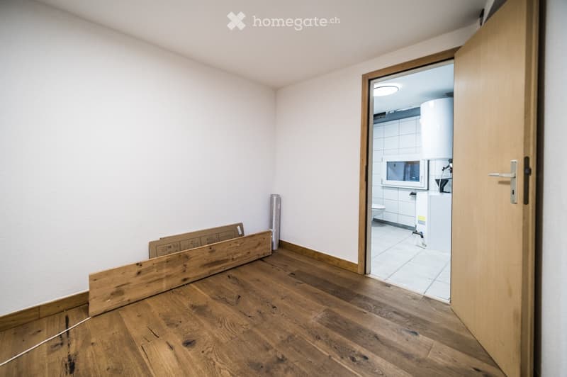 Empty room with wooden flooring and white walls, featuring an open doorway leading to a tiled bathroom with a toilet and sink.