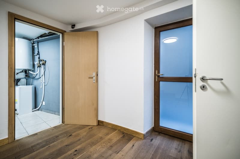 Empty room with wooden flooring, white walls, and a door leading to a utility area with a washing machine and water heater.