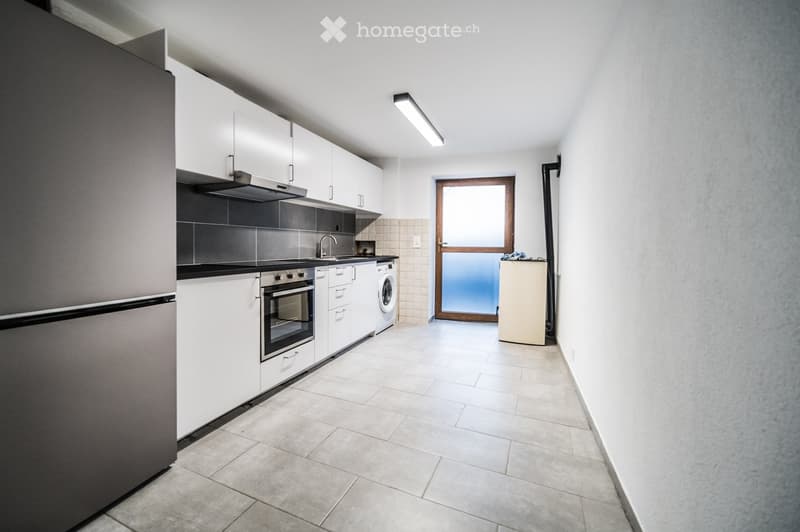 Modern kitchen with white cabinets, stainless steel appliances, and tiled backsplash. Features a refrigerator, oven, sink, washing machine, and range hood.