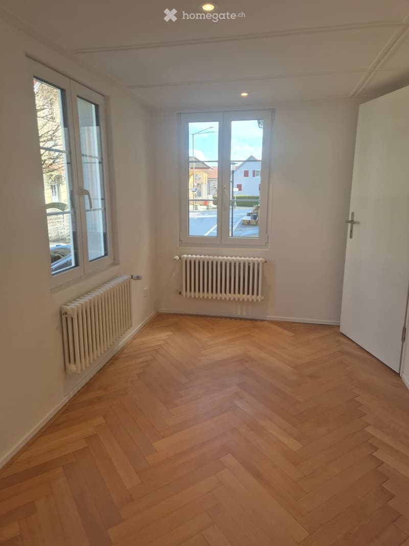 empty room, wooden parquet floor, white walls, two windows, two radiators, open door
