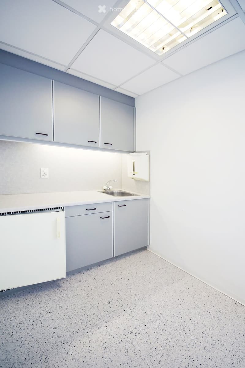 Empty kitchen with white cabinets, a sink, and a refrigerator, featuring a speckled concrete floor and a skylight above.