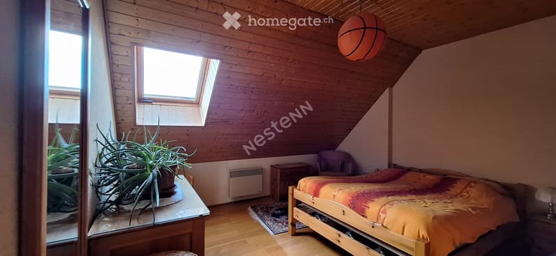 Cozy attic bedroom with wooden walls and ceiling, featuring a bed with colorful bedding, a nightstand, a small table with plants, and a hanging lamp shaped like a basketball.