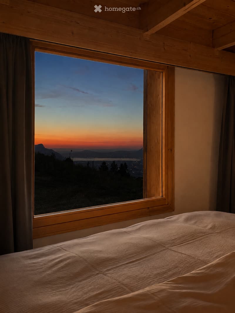 Cozy bedroom with a large window showcasing a scenic sunset view over a landscape, featuring a neatly made bed.