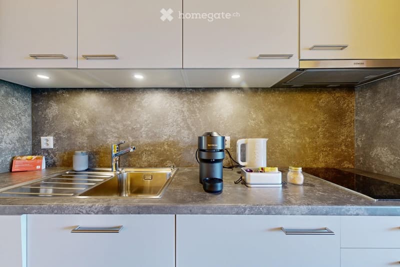 Modern kitchen with white cabinets, stainless steel sink, coffee maker, kettle, and various small appliances on the counter.