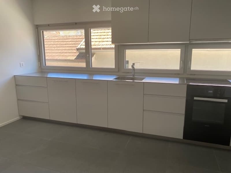 Modern kitchen with white cabinets, dark countertops, and a sink with a faucet. The space features large windows offering a view of a tiled roof.