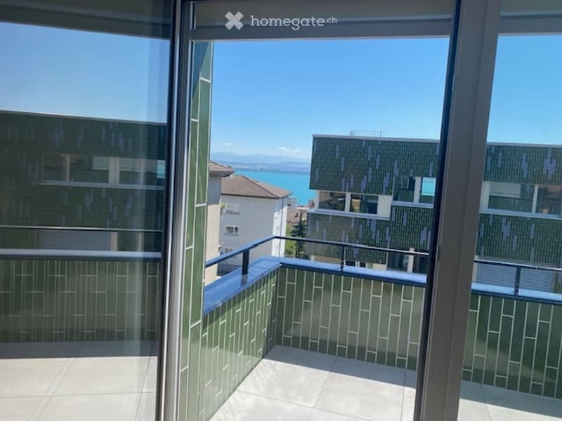 Balcony with modern green tiled railing, overlooking a scenic lake and surrounding buildings.