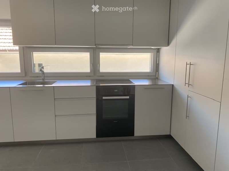 Modern kitchen with white cabinets, stainless steel appliances, and a dark tiled floor. Features a sink, faucet, and oven.