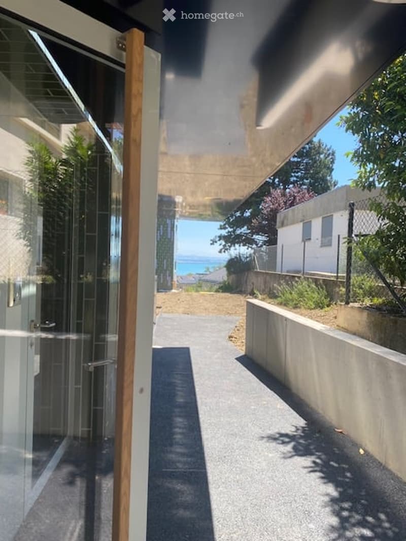 Modern covered walkway leading to an outdoor area with ocean view, concrete walls, glass door, and greenery.
