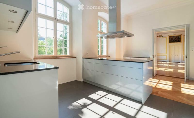 Modern kitchen with white cabinets, stainless steel sink, range hood, and large windows allowing natural light to fill the space.