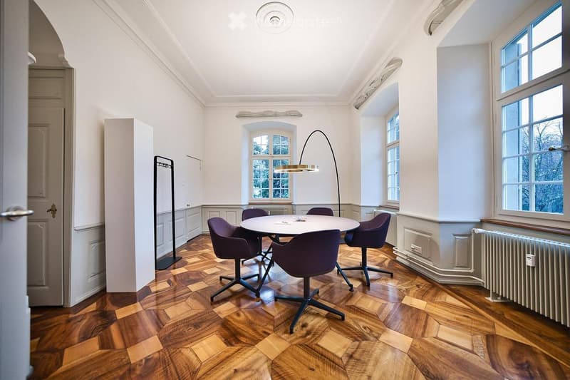 Elegant room with herringbone wooden flooring, white walls, large windows, a round table with six purple chairs, and a modern floor lamp.
