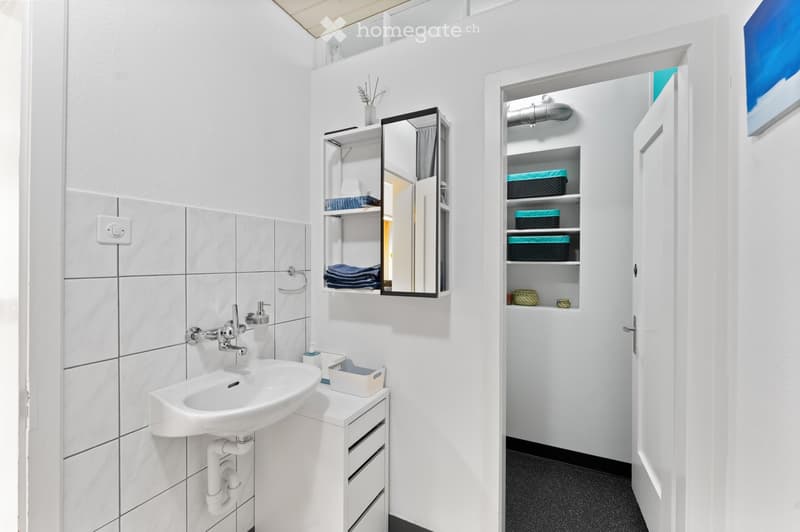 Modern bathroom with white tiles, a sink, a mirror cabinet, and a built-in storage cabinet with shelves and baskets.