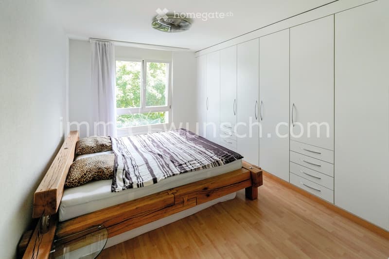 Modern bedroom with a wooden bed frame, striped bedding, leopard-print pillows, white built-in wardrobes, and large windows with curtains.