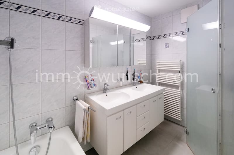 Modern bathroom with a double sink, large mirror, bathtub, radiator, and towel racks.
