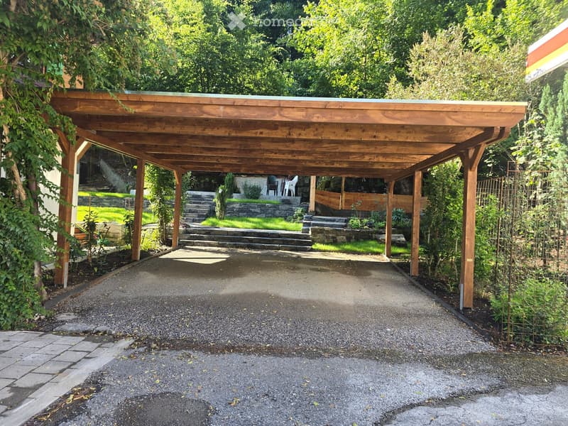 Wooden carport with a gravel driveway, surrounded by greenery and a stone staircase leading to a garden area.
