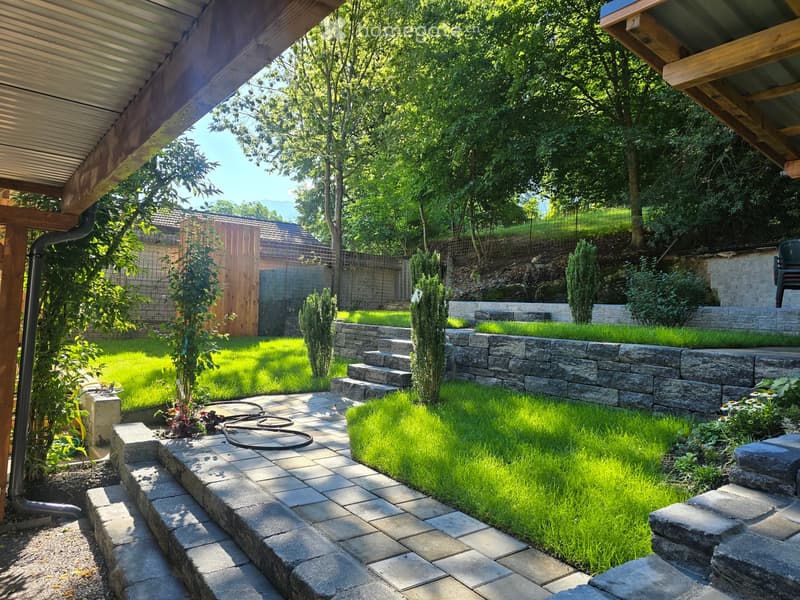 Well-maintained garden with stone steps, lush green grass, small trees, and a wooden fence in the background.