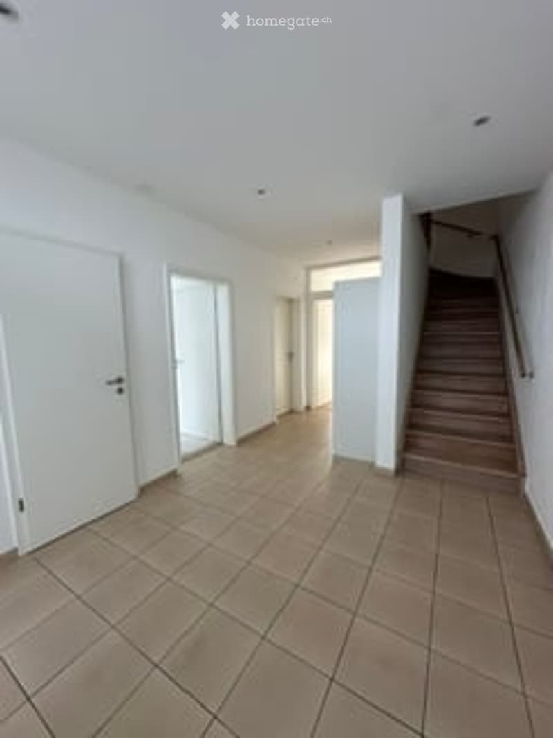 Empty room with tiled floor, white walls, and a staircase leading upwards.