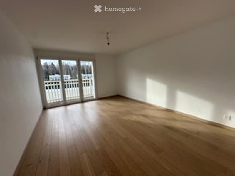Empty room with wooden flooring, white walls, large sliding glass door leading to an outdoor area, and natural light streaming in.