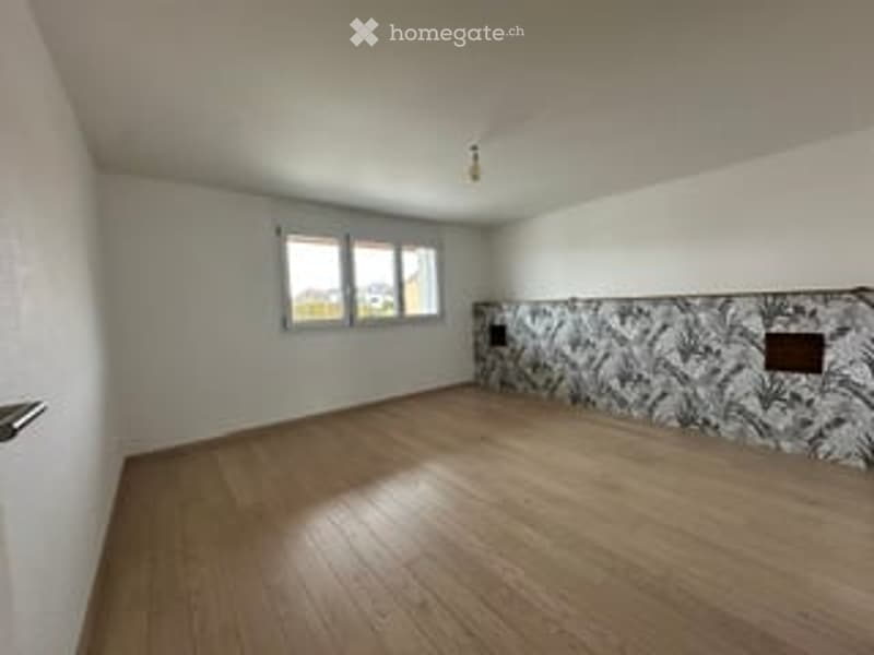 Empty room with wooden flooring, white walls, and a window with multiple panes. The room features a decorative tile backsplash on one wall.