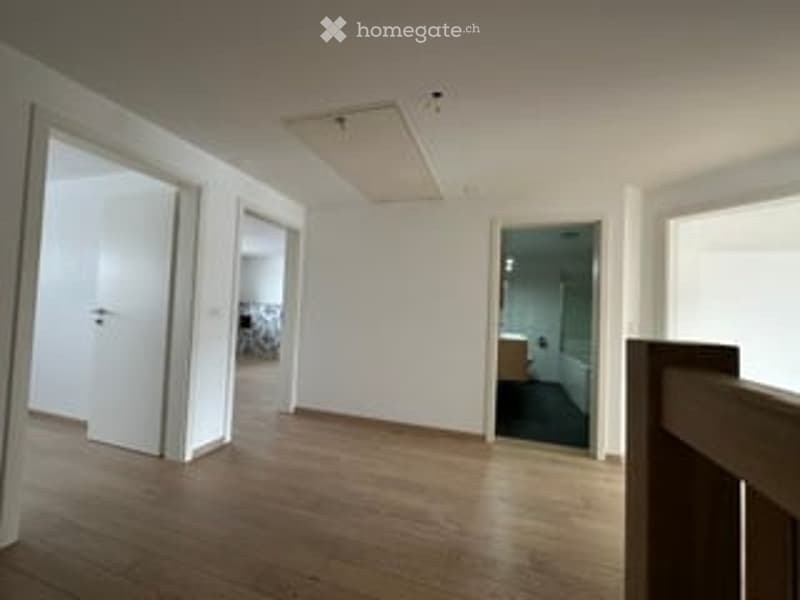 Empty room with wooden flooring, white walls, and multiple doorways leading to other rooms.